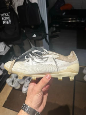  Adidas predator Y3 collab  - Säljer ett par vita Adidas fotbollsskor med grå detaljer och snörning. Skorna har en platt sula med dobbar för gräsplan och en svart tunga med vit autograf. Ovandelen är tillverkad i syntetmaterial och textil för bra komfort och passform.