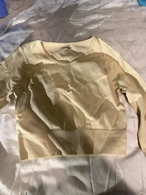 Ribbad kroppad topp💫🌟 - Säljer en ribbad beige långärmad tröja från Gina Tricot i storlek M/L. Tröjan har rund halsringning och bredare ribbad kant nedtill. Materialet är mjukt och stretchigt, likt träningsmaterial. Använd en gång. Enkel och clean design som funkar till många olika stilar.🌟✨