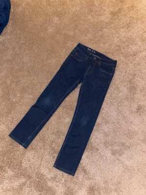 Mörkblå smala jeans Lindex strl 140 - Säljer ett par mörkblå jeans från Lindex i modellen Narrow, storlek 140. Klassisk femficksdesign med smal passform och snygga kontrastsömmar. Perfekta till vardags och lätta att matcha med olika stilar.
