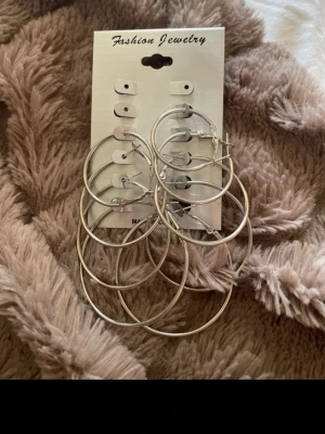 Ingen väst på bilderna - Bilderna visar ett set med stora silvriga örhängen i olika storlekar, men ingen väst finns med.