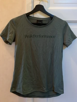 Grön Peak Performance t-shirt XS - Snygg grön t-shirt från Peak Performance i storlek XS. Klassisk rund hals och korta ärmar, med diskret logga tryckt på bröstet. Perfekt för dig som gillar enkel och stilren design. Materialet känns mjukt och bekvämt mot huden.