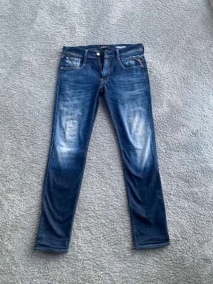 Replay jeans - Anbass slim fit - Säljer ett par blå Replay jeans – modell Anbass Slim Fit, storlek 32. Jeansen är i väldigt bra skick, sparsamt använda och utan slitningar, fläckar eller andra defekter. Replay Anbass är en populär modell med slim fit-passform som sitter snyggt utan att kännas för tight. Klassisk blå färg som funkar till det mesta – perfekt både till vardag och mer uppklädda tillfällen. 