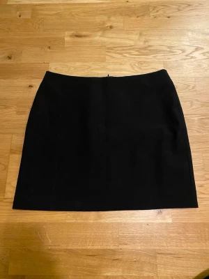 Svart kortkjol  - En stilren svart kortkjol från Mango med diskret dragkedja bak. Kjolen är enkel och lätt att matcha med olika toppar och accessoarer. Perfekt för dig som gillar minimalistisk stil.