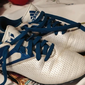 Adidas Messi 15.3 Fotbollsskor [stl. 37+1/3] - Snygga fotbollsskor från Adidas i vitt och blått med coolt mönstrad ovandel och blå snörning. Skorna har en slitstark syntetisk yta och mönstrad sula med dobbar för grymt grepp på planen. Perfekt för dig som vill sticka ut med stil på matchen.
