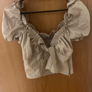 Beige blus med puffärmar och knyt - Supersöt beige blus med puffiga korta ärmar och volangdetaljer längs halsringningen. Använd 1 gång