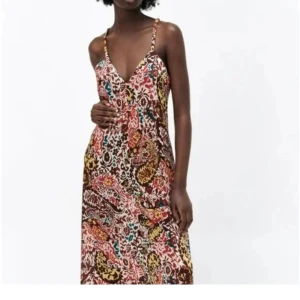 Mönstrad klänning med v-ringning från Zara - Säljer en färgstark långklänning med blommigt mönster i rött, brunt, gult och turkost. Klänningen har v-ringning, smala axelband som korsas i ryggen och ett flowigt fall. 