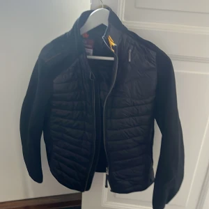 Svart jacka Parajumpers Y-M - Obs barn storlek                                              Tjena ska sälja en del jackor och tröjor framöver, kolla gärna på min andra annonser       Svart quiltad jacka från Parajumpers med coolt gult band vid kragen och broderad logga på ärmen. Jackan har dragkedja framtill, en bröstficka med dragkedja och är tillverkad i syntetmaterial. Perfekt för dig som gillar stilren och sportig look.