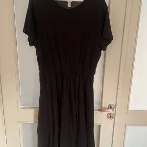 Svart långklänning från H&M L.O.G.G - Svart långklänning från H&M L.O.G.G i storlek XL. Klänningen har rund halsringning, korta ärmar och ett elastiskt midjeparti som ger en snygg siluett. Tillverkad i mjuk bomull som känns skön mot huden. Perfekt för dig som gillar enkel och stilren design.