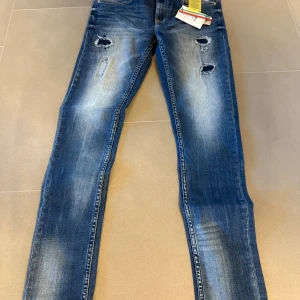 Blå slitna jeans från Vespino - Snygga blå jeans från Vespino med slitna detaljer och hål på låren och knäna. Jeansen har en klassisk femficksdesign, knapp och dragkedja i midjan samt en tvättad look med ljusare partier. Passar dig som gillar streetstyle och en avslappnad vibe.