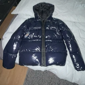 Mörkblå pufferjacka från SikSilk - Säljer en mörkblå, glansig pufferjacka från SikSilk i storlek M. Jackan har huva, dragkedja framtill och är vadderad för extra värme. Perfekt för kalla dagar. Har använt denna max 2gånger. 