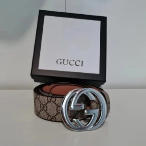 GG Supreme bälte med silverdetalj - Snyggt GG Supreme bälte i brunt med klassiskt monogrammönster och stor silverfärgad GG-spänne. Tillverkat i exklusivt skinn och levereras med originalbox och certifikat. Perfekt accessoar för att lyfta din outfit.