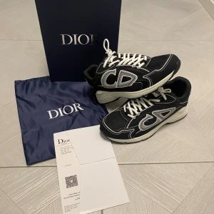 Dior skor - (Kan fixa fram en dior påse för skorna) Snygga svarta sneakers med stora vita CD-loggor på sidorna. Skorna har vit sula, svarta och vita detaljer samt vita skosnören. Ovandelen är i mesh och syntet med coola kontrastsömmar. Perfekta för dig som vill sticka ut med lyxig streetstyle.
