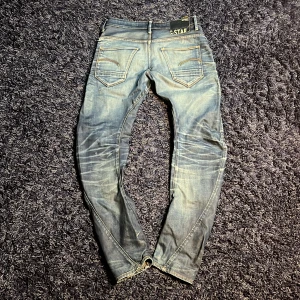 G-star jeans - Säljer ett par blå G-Star Arc 3D Slim jeans med snyggt slitna detaljer och cool faded effekt. Modellen har klassiska fem fickor, markerade sömmar och en slim passform som sitter riktigt schysst. Jeansen är tillverkade i jeansmaterial och har G-Star patch bak, har sköna detaljer som slitningar i fickan och metaltag på bakfickan