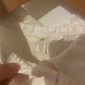 Vit skjorta från H&M i bomull - Klassisk vit skjorta från H&M i storlek M. Skjortan har lång ärm, knappar framtill och en snygg krage. Tillverkad i mjuk bomull som känns skön mot huden. Perfekt för dig som gillar en clean och enkel stil.