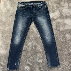 True Religion, Marco, Slim, W32 - Säljer ett par blå True Religion Marco jeans med slim passform. Jeansen har snyggt slitna detaljer, klassisk femficksdesign och ikoniska broderade bakfickor med kontrastsömmar. Materialet är stretchigt denim för extra komfort. Priset är absolut diskutabelt!