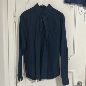 Mörkblå Overshirt/skjorta Dressmann  - Snygg mörkblå skjorta/ overshirt från Dressmann i slim fit-modell. Skjortan har klassisk krage, knappar framtill och en bröstficka. Tillverkad i mjuk bomull, perfekt för dig som gillar stilrena och enkla plagg. Långärmad och passar dig som vill ha en clean look. Bara har använt en gång. Modellen är 180 cm och 67 kg