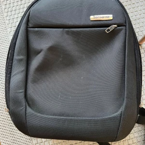 Svart ryggsäck från Samsonite - Snygg svart ryggsäck från Samsonite med flera fack och vadderade axelremmar. Väskan har stilren design, dragkedjor i silverfärg och är tillverkad i slitstark polyester. Perfekt för skola, jobb eller resor när du vill ha med dig allt du behöver.