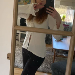 Vit långärmad tröja design by si - Säljer en vit långärmad tröja från design by si, med snygg knytning framtill och lätt utsvängda ärmslut. Tröjan har en feminin v-ringning som ger en fräsch och stilren look. Köpt för 400