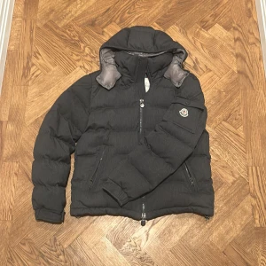 Svart Moncler pufferjacka med huva - Säljer en grå Moncler Montgenevre jacka. Jackan är i storlek 2. Matrialet på jackan är 100% ull. Vid frågor och funderingar så får ni gärna höra av er!