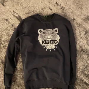 Svart Kenzo sweatshirt  - Svart sweatshirt från Kenzo med ikoniskt broderat tigerhuvud och logga på bröstet. Tröjan har rund halsringning, ribbade muddar och är långärmad. Perfekt för dig som vill sticka ut med en stilren streetwear-look.