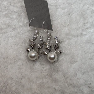 Silvriga örhängen med pärlor och strass - Unika örhängen i silverfärg med dekorativa grenar, glittrande strass och en stor vit pärla som detalj. Perfekta för dig som vill sticka ut med ett coolt och elegant smycke. Hängande modell med krokar för enkel användning.