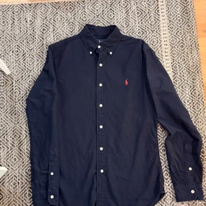  Ralph Lauren Navy Blue Shirt S Size - Selling a navy blue Ralph Lauren shirt in a slim fit with a classic collar and white buttons. The shirt has long sleeves and the iconic red logo embroidered on the chest. Made from soft cotton that feels comfortable against the skin.