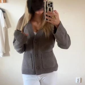 Brun kofta med fickor och knappar - Mysig brun kofta med v-ringning, stora knappar framtill och två rejäla fickor. Koftan har breda ribbade muddar vid ärmslut och nederkant, och är i ett stickat material som känns både stilrent och chill.