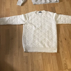 Vit quiltad sweatshirt - Säljer en vit quiltad sweatshirt med rund hals och långa ärmar. Tröjan har ett snyggt rutmönster över hela ytan och är tillverkad i ett mjukt material som känns skönt mot huden. Perfekt för dig som gillar stilrena och trendiga plagg.