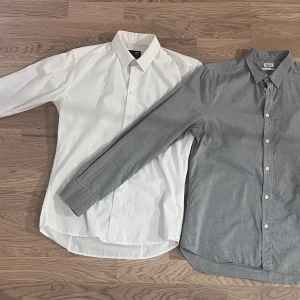 Grå och vit skjorta, storlek S-M - Snygg grå skjorta från Filippa K i klassisk modell med krage och vita knappar. Skjortan är långärmad passar perfekt till jeans eller kostymbyxor. Snygg vit skjorta från Minimum. Båda skjortorna är i samma storlek.
