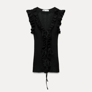 Svart ribbad topp med volanger från Zara - Säljer en svart ribbad topp från Zara med djup v-ringning, volanger längs axlar och hals samt snörning framtill. Toppen är ärmlös och har en croppad passform som ger en cool och trendig vibe. Perfekt för dig som gillar detaljer och vill sticka ut.