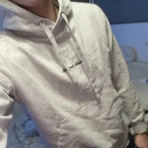 Ljusgrå hoodie Originals Studio - Ljusgrå hoodie från Originals Studio med broderad svart logga på bröstet. Klassisk modell med huva, snörning och stor magficka. Mjuk och skön, perfekt för chill dagar. Långärmad och normal passform. 