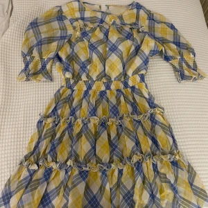 Rutig sommarklänning Michael Kors M - Säljer en söt rutig klänning från Michael Kors i storlek M. Klänningen har blå, gula och vita toner, volangdetaljer och smock i midjan och vid ärmslut. Den har korta ärmar och är tillverkad i ett lätt bomullstyg, perfekt för varma dagar. Inte använd en ända gång. Köpt för: 4900kr