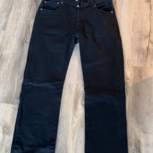 Svarta Levi's 501 jeans straight fit. Storlek W34 L32 - Klassiska svarta Levi's 501 jeans med raka ben och femficksmodell. Jeansen har knappgylf, läderpatch bak och är tillverkade i kraftig bomullsdenim. Perfekta för dig som gillar en tidlös och clean look.