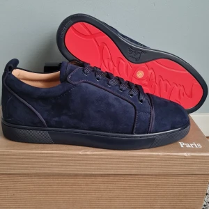 Mörkblå sneakers från Christian Louboutin - Snygga mörkblå sneakers i mocka från Christian Louboutin med ikonisk röd sula. Skorna har rund tå, platt sula och klassisk snörning. Perfekta för dig som vill sticka ut med exklusiv stil och detaljer.