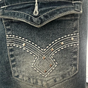 Blå jeans med broderade bakfickor (pris kan diskuteras) - Snygga blå jeans med coola broderade detaljer och nitar på bakfickorna. Jeansen har klassisk femficksdesign, silverfärgade knappar och en lätt tvättad look. Perfekta för dig som gillar en unik touch på dina jeans.