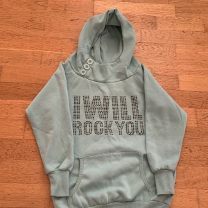 Ljusblå hoodie från Miss Snob - Ljusblå hoodie från Miss Snob med texten 'I WILL ROCK YOU' i glittriga stenar framtill. Tröjan har tre knappar vid halsen och är super snygg💗