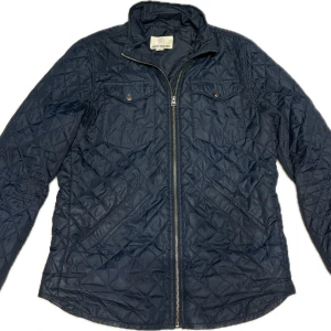 Mörkblå quiltad jacka Shine Original - Quiltad mörkblå jacka från Shine Original med dragkedja framtill, två bröstfickor med knappar och snedställda sidfickor.