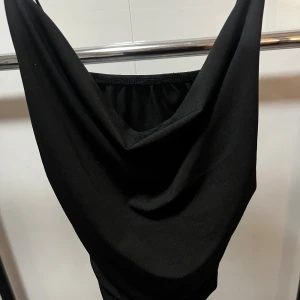 Svart tight topp med drapering - Svart topp med smala axelband och snygg drapering framtill. Toppen har en tight passform och är sydd i ett stretchigt material som formar sig efter kroppen. Perfekt för dig som gillar minimalistisk och stilren look.