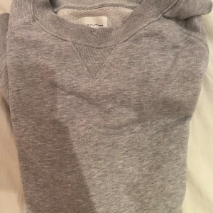 Grå sweatshirt från Gant Rugger - En klassisk grå sweatshirt från Gant Rugger i storlek M. Tröjan har rund halsringning, ribbade muddar och är tillverkad i mjuk bomull. Perfekt för en chill och stilren look, enkel att matcha med jeans eller joggers.