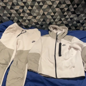 Nike vit och grå vindjacka med huva - Nike vindjacka i vitt och ljusgrått med huva och hel dragkedja framtill med matchande byxor till 