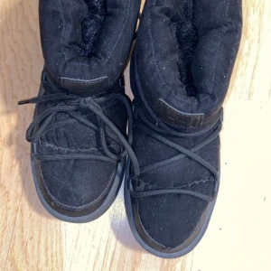 Svarta moon boots med snörning - Säljer ett par svarta moon boots från INUIKII med grov platt sula och snörning runt hela skon. Utsidan är i mocka och insidan är fodrad för extra värme. Perfekta för kalla vinterdagar och har en chunky look som sticker ut.