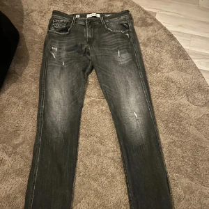 Replay svarta skinny jeans med slitningar - Snygga svarta skinny jeans från Replay med slitna detaljer och diskret tvättad look. Klassisk femficksmodell med dragkedja och knapp. Jeansen har tydliga sömmar och bakfickor med Replay-logga. Perfekta för en cool och avslappnad stil.