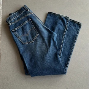 Levi's 551 blå jeans W29 L32 - Säljer ett par klassiska Levi's 551 jeans i blå denim. De har raka ben, fem fickor och snygga kontrastsömmar. Märket syns tydligt på bakfickan och läderpatchen bak. Perfekta för dig som gillar tidlös stil och vill ha ett par jeans som funkar till allt.