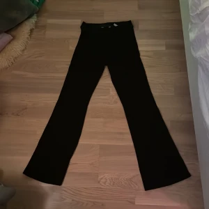 Svarta bootcut byxor med stretch - Säljer ett par svarta bootcut byxor med inte så hög midja och stretchigt material. Byxorna har en klassisk siluett med utsvängda ben och är perfekta för dig som gillar en stilren look. Passar till många olika outfits och är riktigt bekväma. Inga jeans, 164 storlek 13-14 år