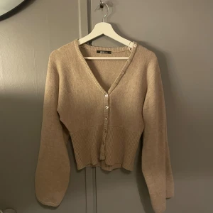 Beige kofta från Gina Tricot - Superfin beige kofta från Gina Tricot med v-ringning och knappar som design, lite ballong aktiga armar. Använd en gång!