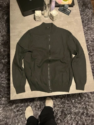 Svart kofta med dragkedja Massimo Dutti - Snygg svart kofta från Massimo Dutti med hel dragkedja framtill och ribbad krage. Tröjan är långärmad och har ribbade muddar vid ärmslut och nederkant. Materialet är mjukt och känns lyxigt, perfekt för kyliga dagar.