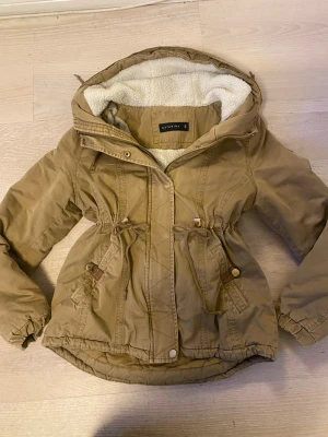 Beige tjock jacka med teddyfoder!!🥰🥰 - Säljer en beige parkajacka från Catarina i storlek S. Jackan har mysigt vitt teddyfoder i huvan, dragsko i midjan och praktiska fickor med knappar. Man drar åt den med ett snöre i midjan:))💗💗🫰