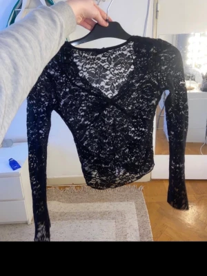 Svart spetsblus från Gina Tricot - Säljer en svart långärmad blus från Gina Tricot i storlek XS. Blusen är helt i spets med v-ringad hals och figurnära passform. Perfekt för dig som gillar detaljer och vill ha en snygg topp med genombrutet mönster.