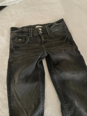 Svarta bootcut jeans med dubbla knappar - Snygga svarta jeans med bootcut passform och dubbla knappar i midjan. Jeansen har klassisk femficksdesign, kontrastsömmar och är tillverkade i jeansmaterial. Perfekta för dig som gillar en lite utsvängd look och vill ha en cool stil.