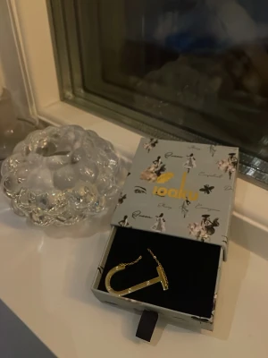 Halsband med J - Jag säljer nu ett halsband med ett stort J i guld med små stenar i rostfritt stål. En av stenarna har ramlat av men det är inget man märker tydligt. Nypris 500kr, från ioaku. Hör av vid eventuella frågor💗💗